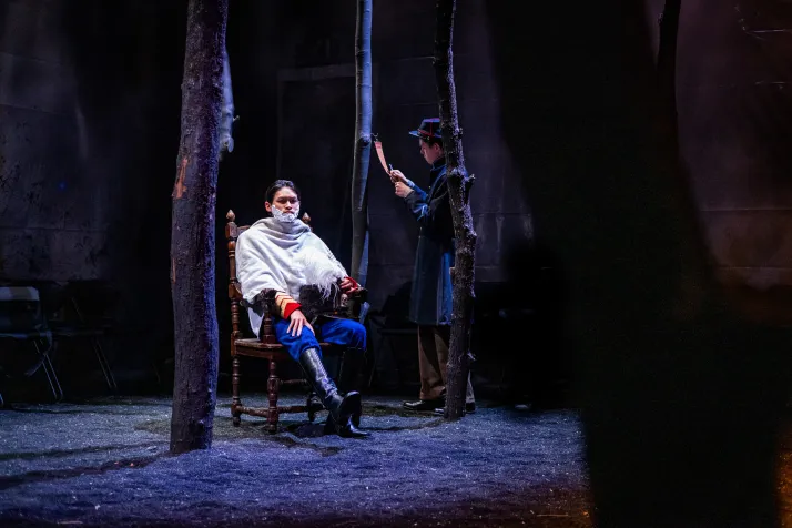 A man is sitting in a chair with shaving cream on his face, while another speaks down to him 