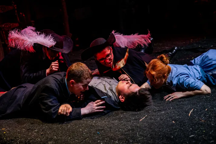 Several people crawl on their bellies towards Woyzeck who stares up at the sky on his back 