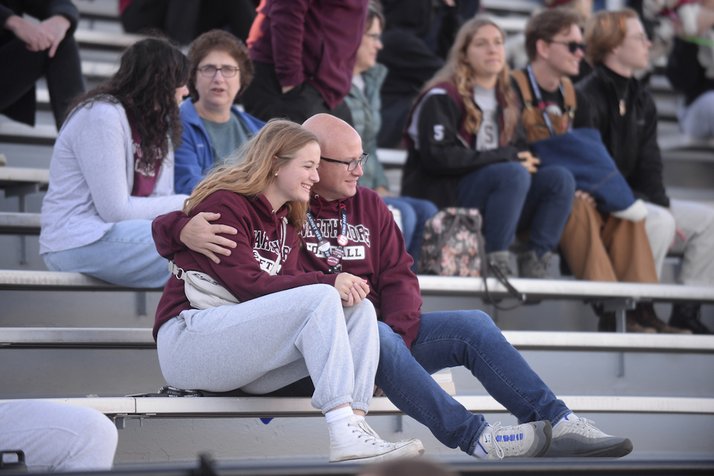 Father and daughter sit in bleachers at game