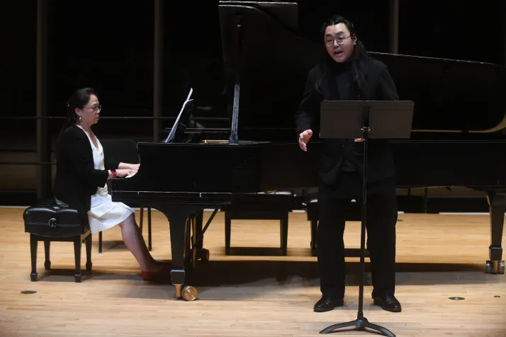 Person sings while standing in front of piano played by accompaniment