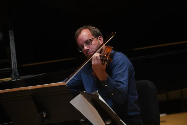 Person sits on stage playing violin or viola