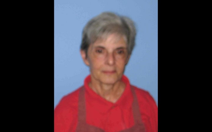Headshot of an older woman with short grey hair, wearing a red polo shirt and an apron.