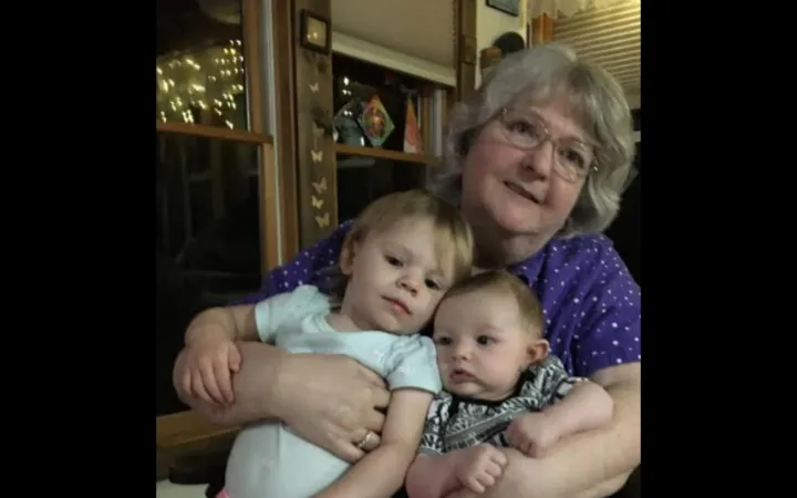 Woman with grey hair and bangs holds two small children.
