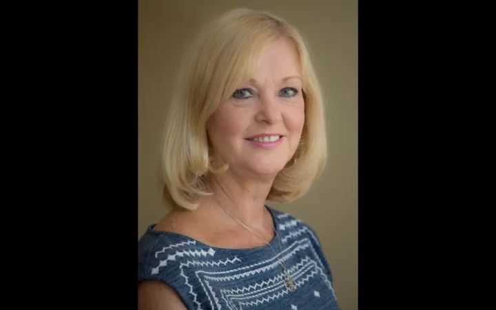 Head shot of a woman with shoulder length blonde hair wearing a striped blue shirt and blue eyeshadow.