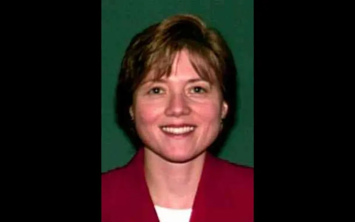 Headshot of a woman with short brown hair and bangs who is wearing a red blazer and white top.