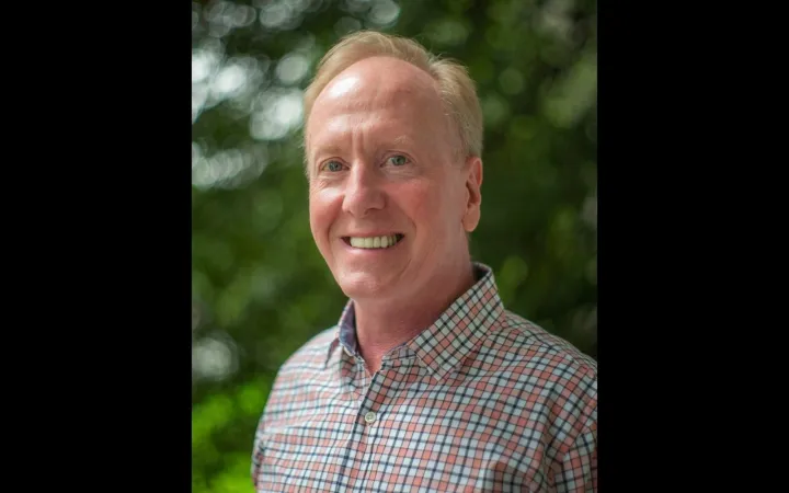 Head shot of a smiling man with short blonde hair and a checkered shirt.