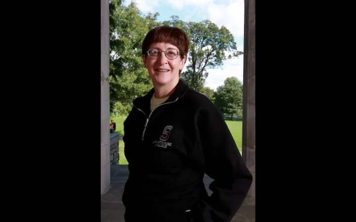 Woman with short brown hair and glasses stands outside in a dark blue sweater and smiles at the camera.