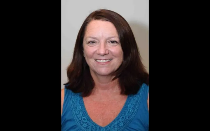 Headshot of a woman with shoulder length dark hair wearing a v-neck teal top.