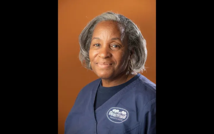 Headshot of a woman with salt and pepper shoulder length hair wearing a navy blue polo shirt.