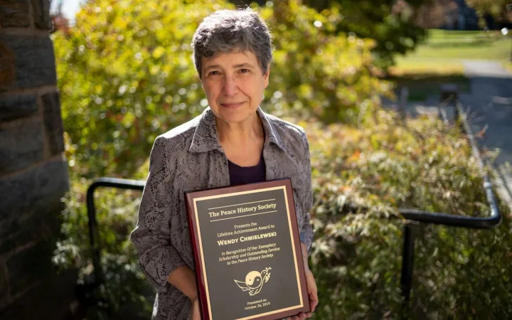 Woman with close cropped dark hair stands outdoors and holds a plaque while she smiles at the camera.