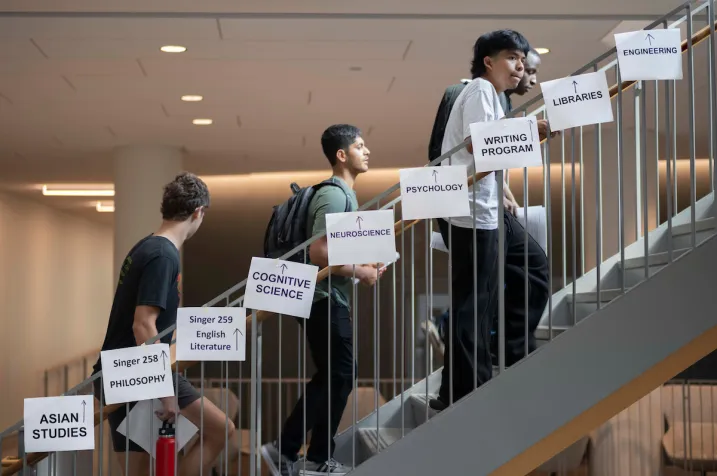 Students climb up steps. Taped to the steps are white pieces of paper that say "Asian Studies", "Philosophy" and other subjects.