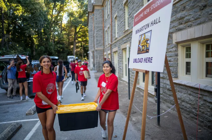 Two orientation team members help carry box during move-in