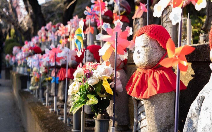 Rows of statues of people interspersed with colorful pinwheels and flowers