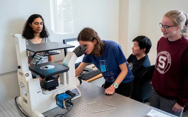 student looking through microscope with 3 students observing