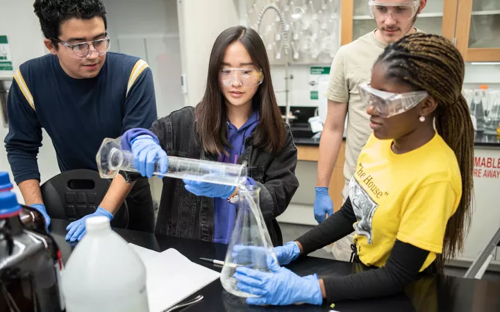 one student pours liquid in a beaker held by another while a third watches