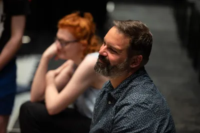 Alex Torra seated in a theater rehearsal, listening attentively to collaborators.