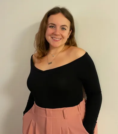 Image of Area Coordinator Erin in a black shirt and pink pants in front of an off white background.