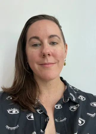 Image Description: a white non-binary person with long brown hair, shaved on one side and wearing a black & white shirt