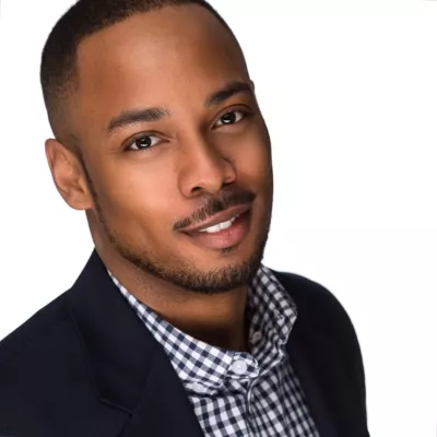 Headshot of Isaiah Matthew Wooden smiling and wearing a navy blazer and blue and white checkered shirt.