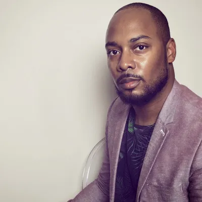 Headshot of Wooden wearing a salmon-colored blazer and a dark shirt with a tropic print.