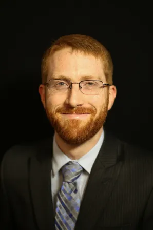 Smiling photograph of Professor Mark Lewis in jacket and tie on a black background