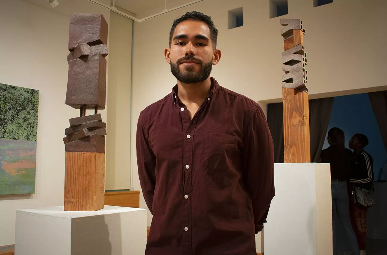 Student stands in front of his sculptures in List Gallery
