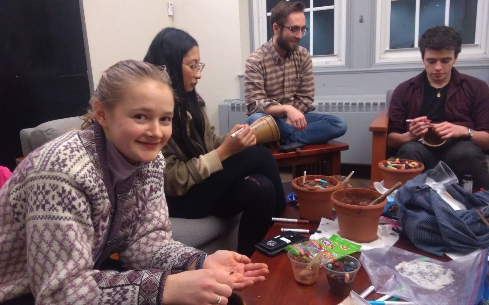 A group of students sit around a table in a dorm lounge covered with craft supplies