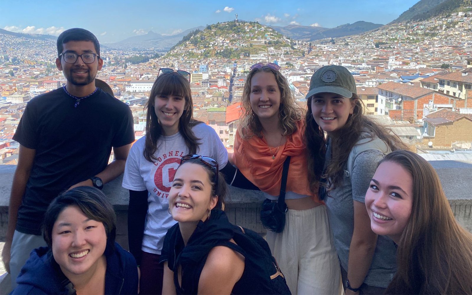 Group of students leaning against a wall on a mountain peak with view of town in background