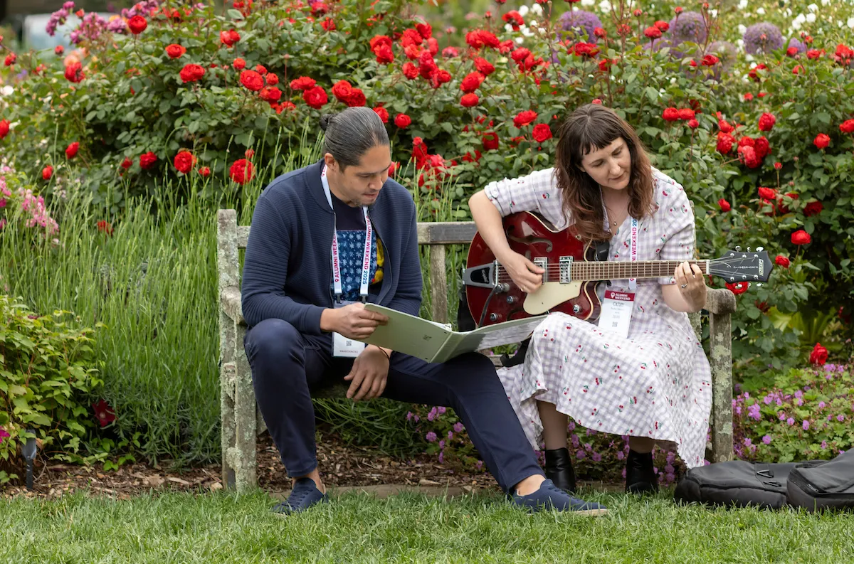 Alums sit on bench and woman plays guita