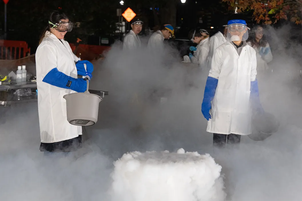 Liquid nitrogen produces large clouds as students wear white lab coats, blue gloves, and goggles