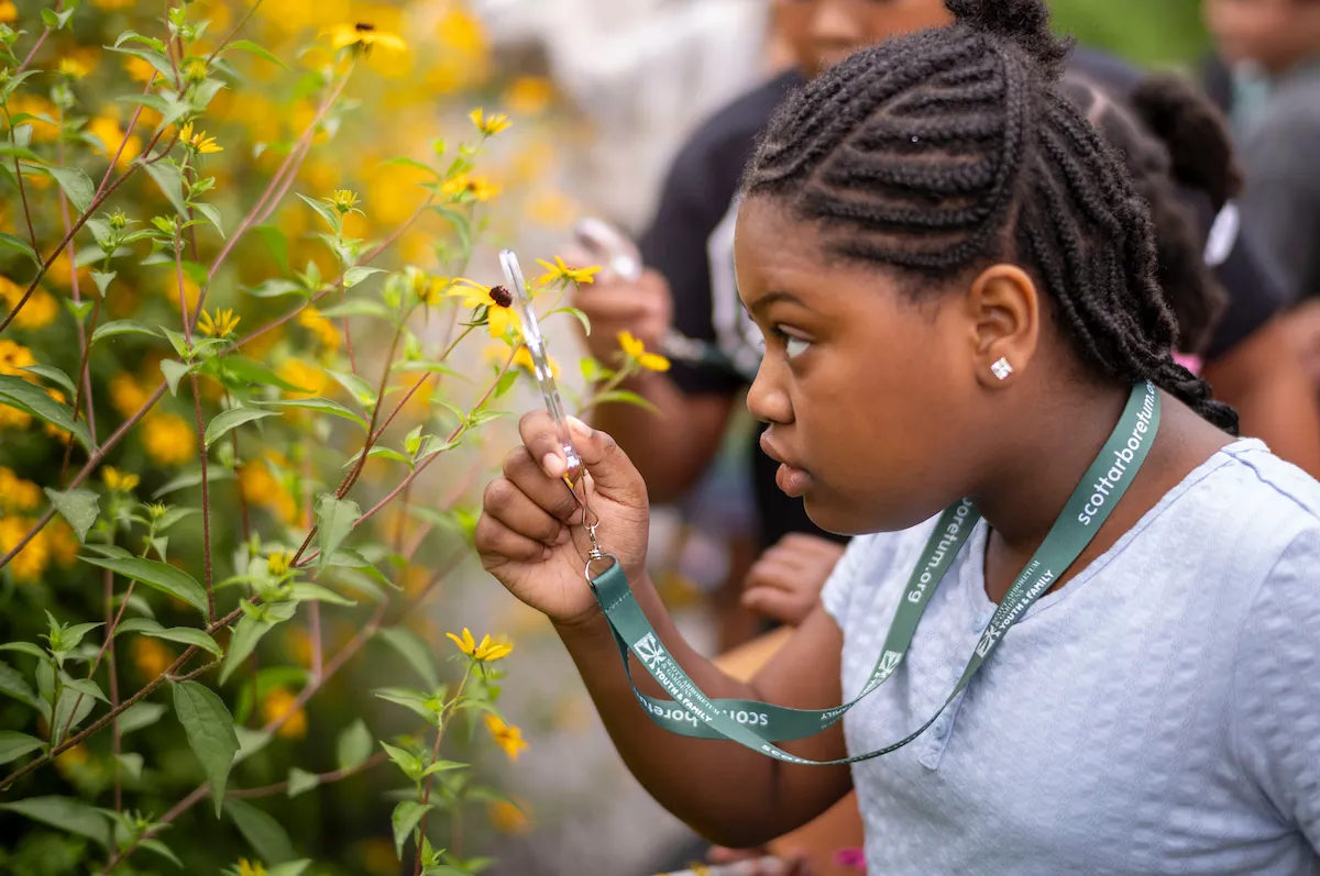 young girl uses a magnifying glass to look closely at a plant outside