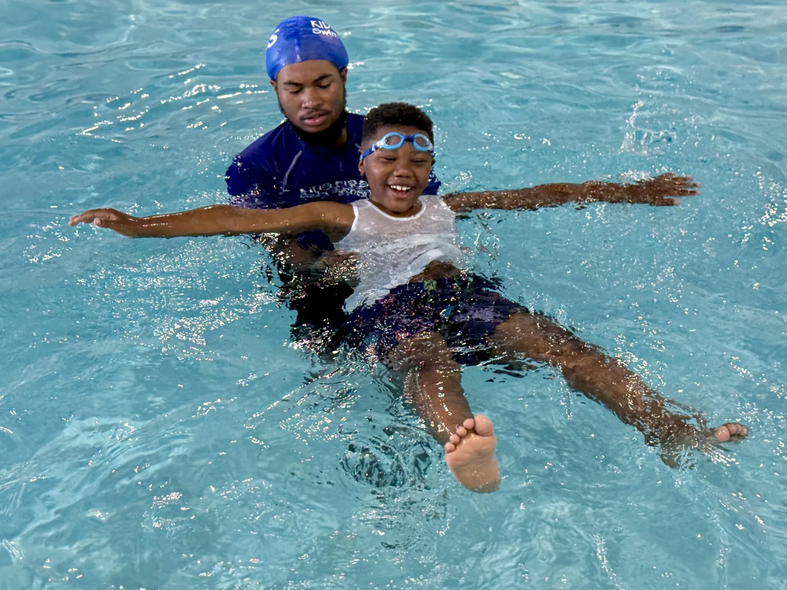 a young boy floats in a pool while being held by a swim instructor