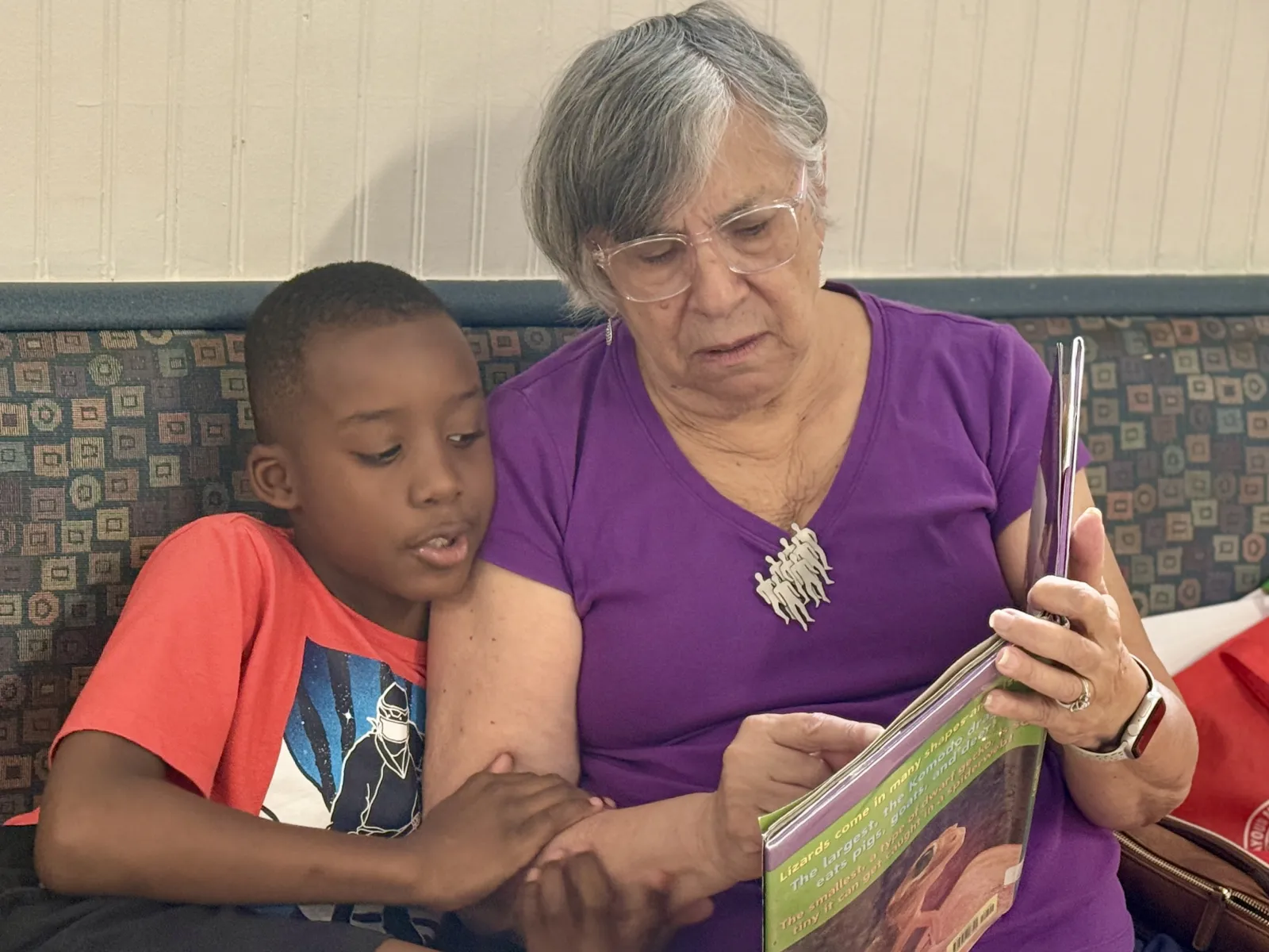 a woman reads a book alongside a third grade boy.