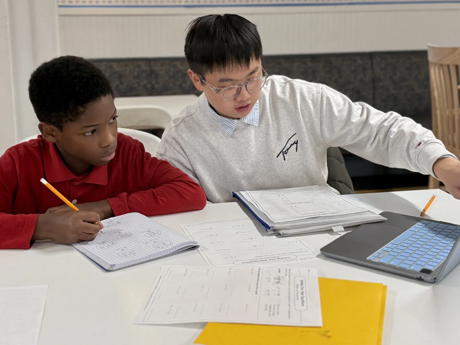 a college student sit next to a middle school boy working on math homework on a laptop