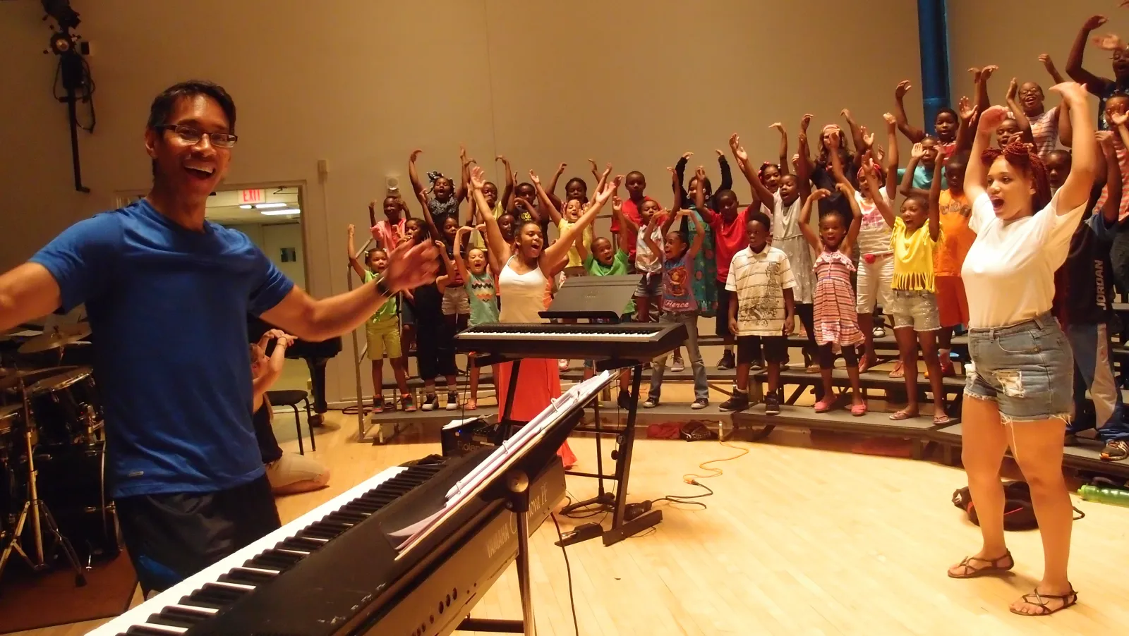 John Alston with outstretched arms in front of a children's choir with the children also stretching their arms up