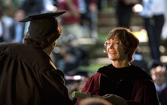 President Rebecca Chopp hands a diploma to a graduating student