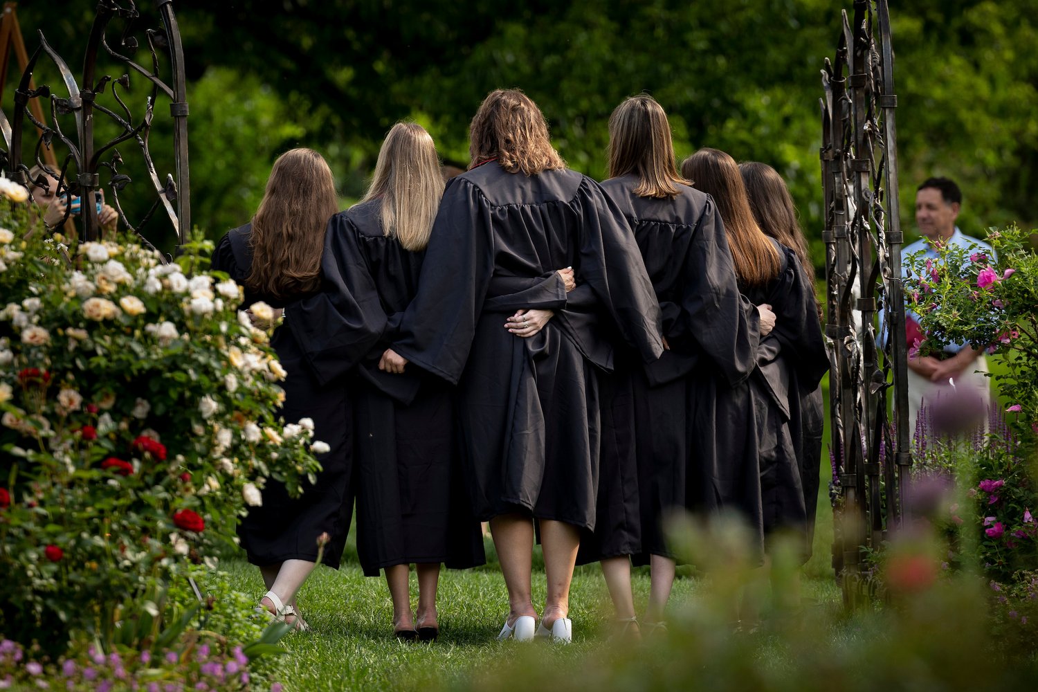Several graduates pose in garden with backs turned to camera