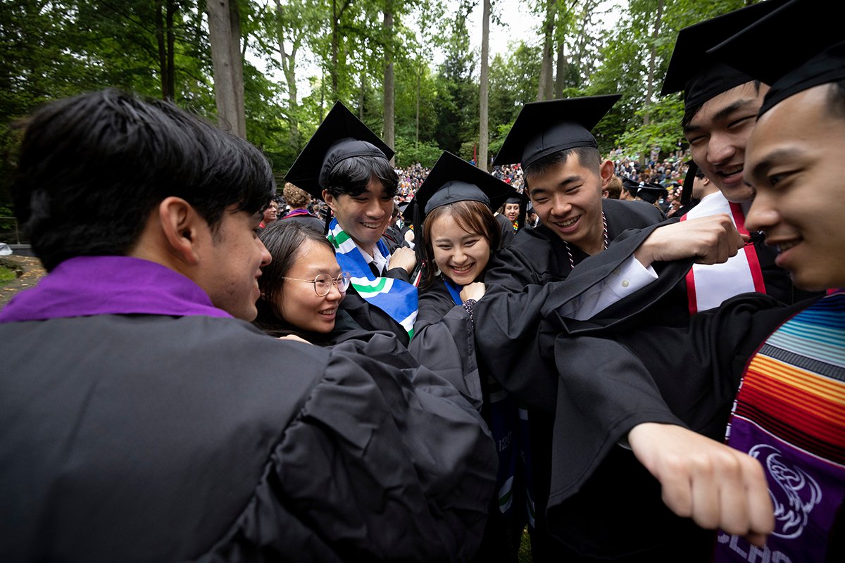 Students wearing caps and gowns bump elbows