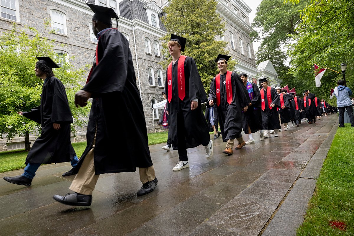 Students walk on rainy day in caps and gowns