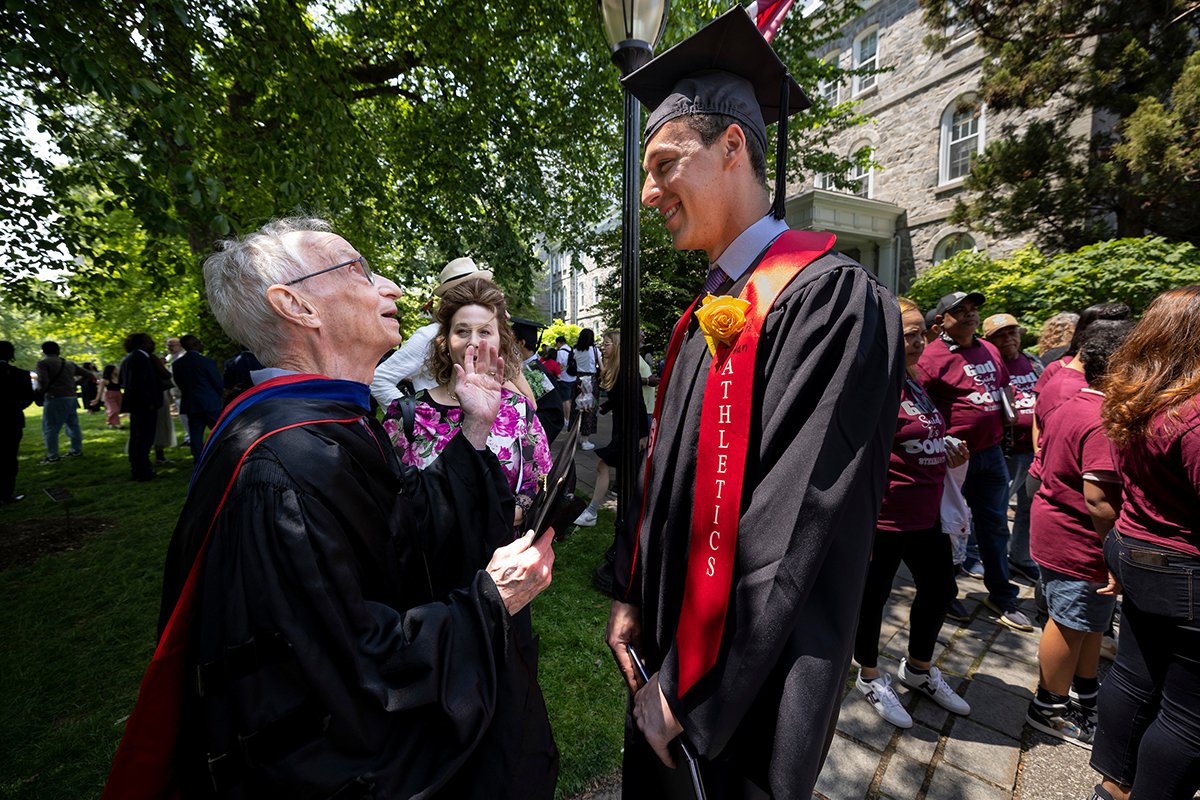 Student wearing cap and gown shakes hand of professor after ceremony
