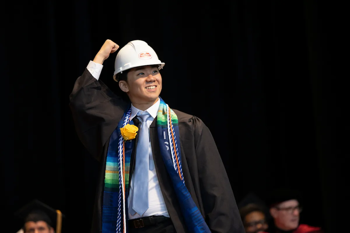 student in white hard hat walks at commencement