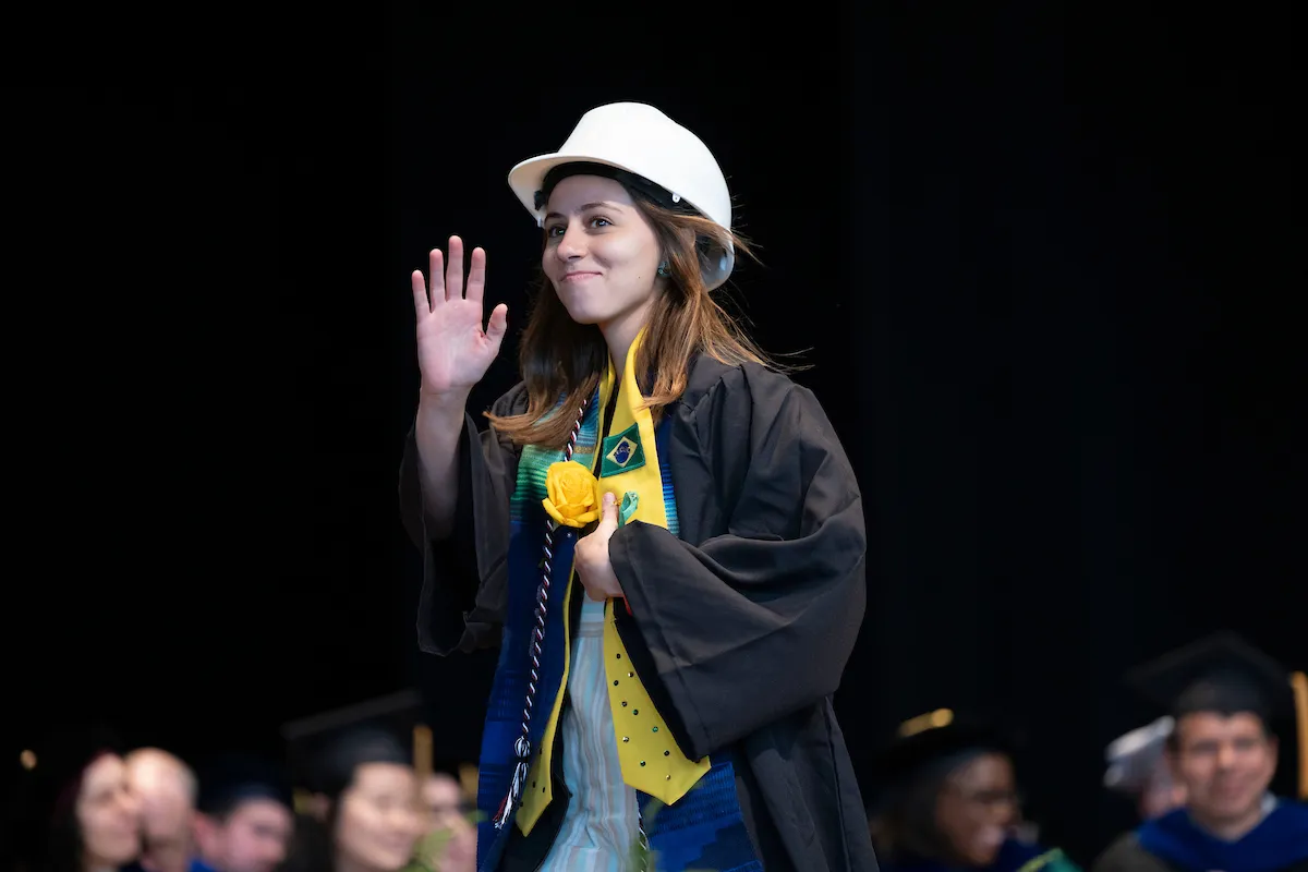 student in white hard hat walks at commencement