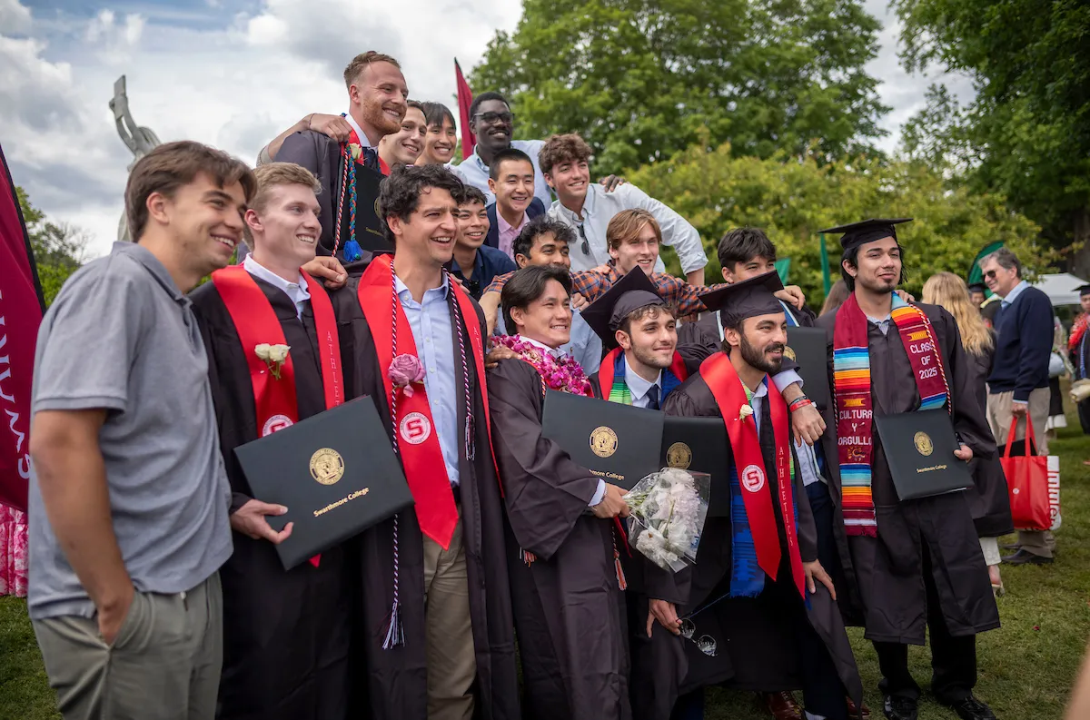 Students celebrate in front of big chair after commencement