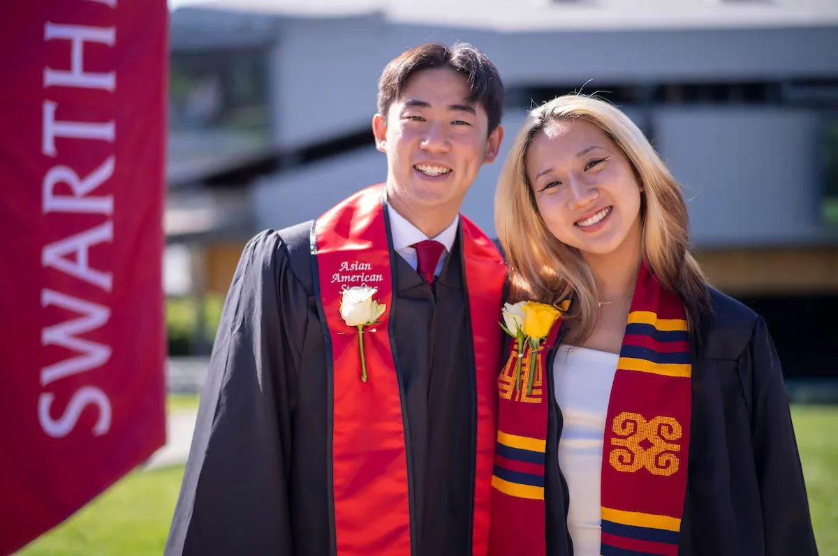 Two students pose in front of Swarthmore banner at commencement