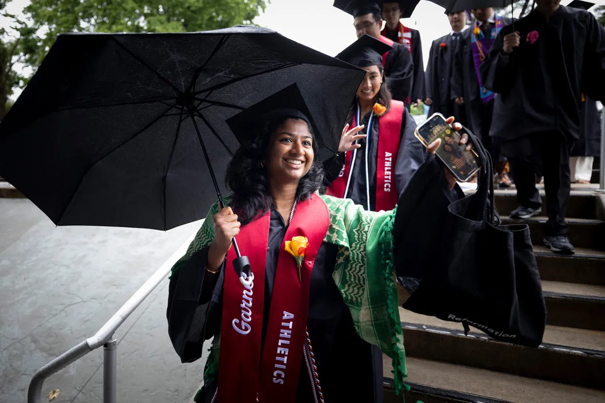 Student holds umbrella during graduation procession
