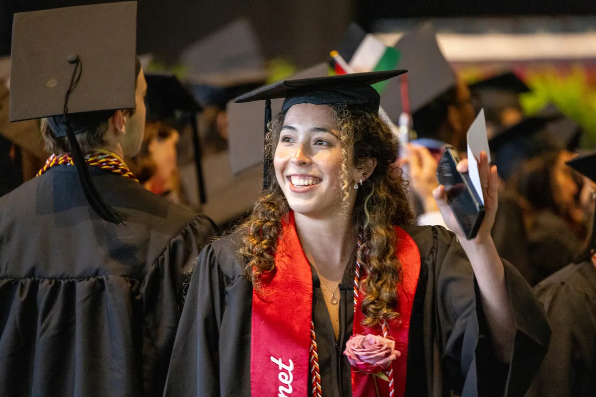 Student smiles and waves at crowd during graduation procession