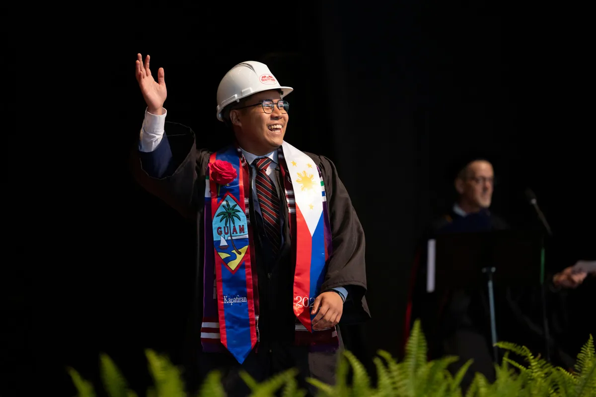 Student in white hard hat waves to crowd