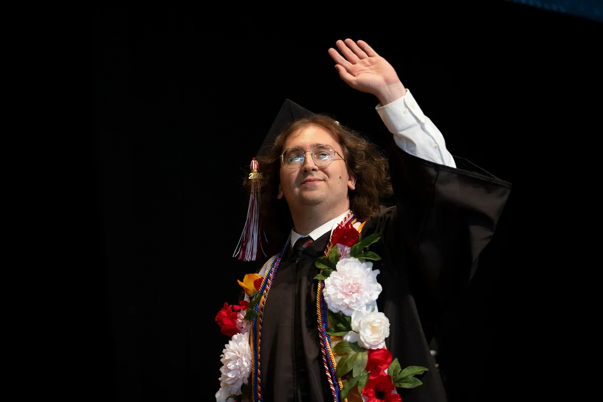 Student waves at crowd while crossing stage