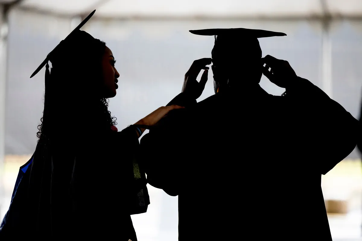 Student helps another student with graduation garb