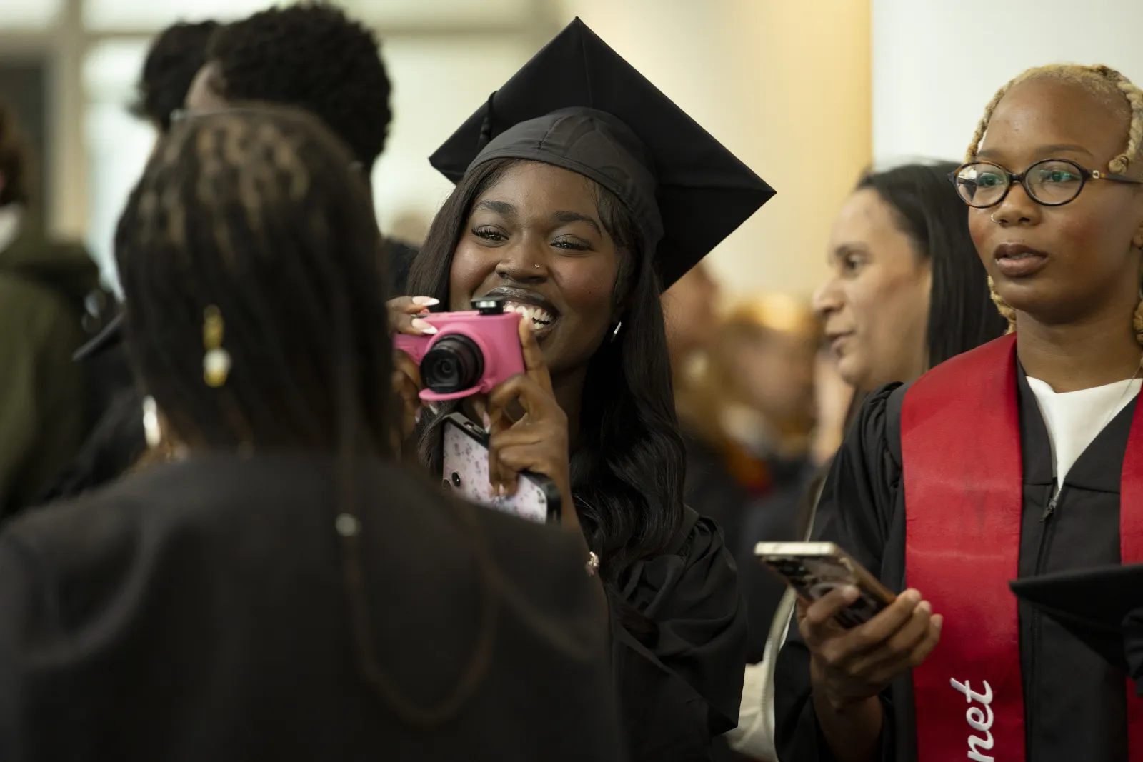 Student with disposable camera takes picture of another student while wearing commencement robes